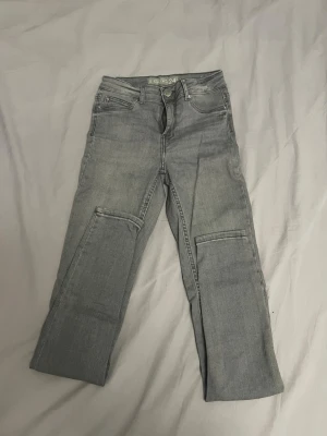Grå skinny jeans från Amisu, W24 - Snygga grå skinny jeans från Amisu med midwaist-passform. Klassisk femficksmodell med dragkedja och knapp framtill. Jeansen är i stretchigt material och har raka ben med diskreta sömdetaljer vid knäna. Storlek 24/XXS