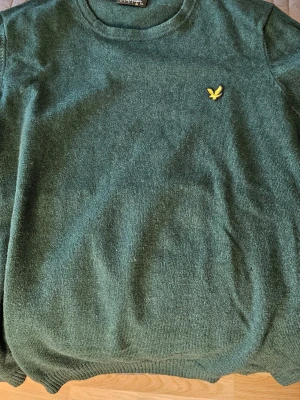 Mörkgrön stickad tröja från Lyle & Scott - Säljer en mörkgrön stickad tröja från Lyle & Scott med klassisk rund hals och den ikoniska gula loggan broderad på bröstet. Perfekt till höst och vinter