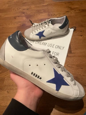 Golden Goose Skor - Snygga sneakers från Golden Goose med den ikoniska mörkblåa stjärnan. Skorna är i bra skick och med skorna kommer dustbag. Modellen heter Superstar och skorna är storlek 42. Skriv ifall ni har fler frågor 💯