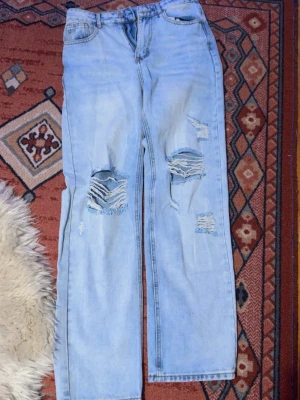 Ljusblåa ripped jeans från SHEIN - Säljer ett par ljusblå jeans från SHEIN i storlek S. Byxorna har raka ben och flera slitningar med stora hål på båda knäna. Klassisk femficksmodell och normal passform. Perfekta till sneakers eller boots. Högmidjade. Bra kvalité för att vara Shein. Inte blivit använda så mycket, men absolut inte nyskick heller. Säljes då jag gått ifrån högmidjat dvs de blir ej använda. 