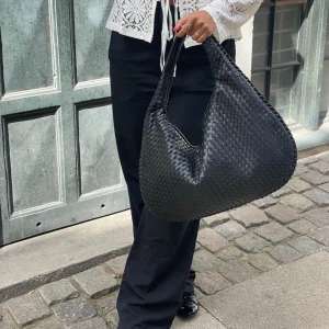 Svart flät svart axelväska i skinn - Säljer en tip top svart axelväska i flätad skinnimitation. Väskan har en mjuk, rundad form och bred axelrem som gör den enkel att bära. Stängs med dragkedja och rymmer allt du behöver till vardagen. Perfekt för dig som gillar stilrena detaljer.