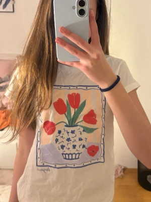 Vit t-shirt med tulpanmotiv - Vit t-shirt från Lindex med ett färgglatt tryck av röda tulpaner i en blåvit vas på bröstet.