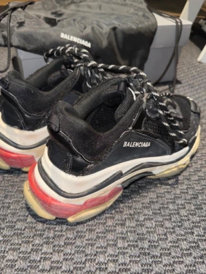 Balenciaga Triple S sneakers  - Säljer ett par Balenciaga Triple S sneakers i svart med vita och röda detaljer. Skorna har chunky sula, rund tå och svart/vita snören. 