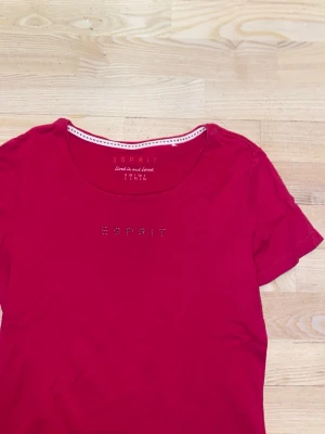 Rosa Esprit t-shirt med strassdetalj - Rosa t-shirt från Esprit med rund halsringning och korta ärmar. Framsidan har Esprit-loggan i små strass-stenar som ger en extra touch. Tillverkad i mjuk bomull som känns skön mot huden. (INTE DEN GRÖNA!, den bilden är bara med för att visa hur tröjan sitter på)