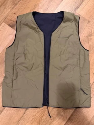 Vändbar dunväst från Peak Performance - Säljer en vändbar dunväst från Peak Performance. Ena sidan är olivgrön och den andra svart, båda med diskret logga på bröstet. Västen har dragkedja framtill och är lätt vadderad för extra värme. Perfekt lager för kyliga dagar.