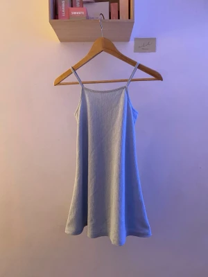 Ljusblå ribbad kortklänning 157 - Supersöt ljusblå kortklänning från 157 med tunna axelband och ribbad struktur. Klänningen har en enkel, flowy passform och är perfekt för varma dagar. Tillverkad i mjukt, stretchigt material som känns skönt mot huden.