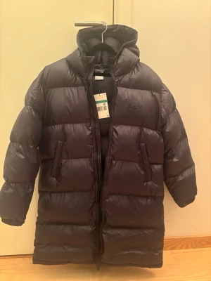 Helt ny Nike vinterjacka - Nike parkas puffer jacka i storlek 158-170/ Barn XL, knälång och luva dock ej avtagbar, två fickor samt två innerfickor, tvåvägsdragkedja.