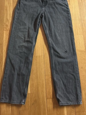 Grå jeans från GANT - Säljer ett par svarta jeans från GANT med klassisk femficksdesign och rak passform. Jeansen har en mörkgrå tvätt och är tillverkade i jeansmaterial. Perfekta för en avslappnad stil.