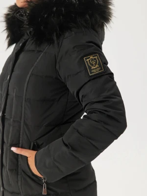 Svart lång pufferjacka med fuskpäls - Säljer en svart lång pufferjacka från GALLA OUTERWEAR med stor huva och fuskpäls. Jackan har dragkedja, knappar och två fickor framtill. Märkespatch på ärmen och quiltad design ger en clean look. Perfekt för kalla dagar.