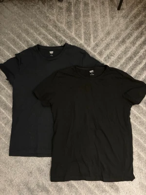 2-pack svarta t-shirts från 157 - Två klassiska svarta t-shirts från 157 med rund hals och korta ärmar. Perfekta basplagg i mjuk bomull som funkar till allt. Enkel och stilren design utan tryck eller detaljer.