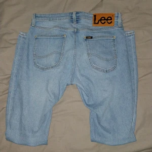 Ljusblå jeans från Lee - Säljer ett par ljusblå jeans från Lee med klassisk femficksdesign, Lee-logga på bakfickan och läderpatch i midjan. Shortsen har normal passform, knapp och dragkedja framtill samt bälteshällor.