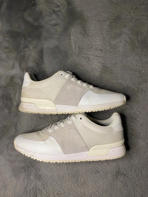 Vita sneakers från Björn Borg - Snygga vita sneakers från Björn Borg med mesh och mockadetaljer på sidorna. Skorna har rund tå, snörning och platt sula med mönstrad undersida. Perfekta för dig som gillar stilrena och ljusa sneakers med sportig vibe.#sneakers #whitesneakers #scandistyle