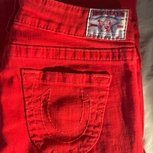 Röda jeans från True Religion - Snygga röda jeans från True Religion med låg midja och bootcut-stil. Skitballa med klar färg och unika design (knapparna är som diamanter. Köpta i köpenhamn i somras men kommer inte jättemycket till användning. 