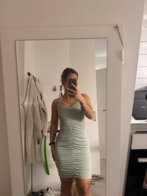 Ljusgrön ribbad kortklänning med snörning - Supersnygg ljusgrön ribbad klänning med smala axelband och snörning på ena axeln. Tight passform och rynkade detaljer framtill som ger en riktigt schysst siluett. Perfekt för dig som gillar en enkel men ändå trendig look.