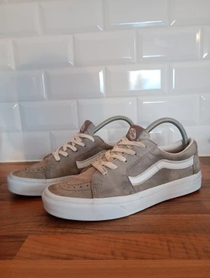 Vans skor - Säljer ett par Vans Old Skool sneakers i grå mocka med klassisk vit sidorand och vit platt sula. Skorna har snörning och rund tå, samt den ikoniska brun/orangea gummisulan med rutmönster. Perfekt för dig som gillar streetstyle och skate-vibe. Vid köp av varan gratis marmor armband!