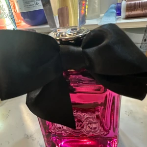 Juicy Couture rosa parfymflaska - Snygg rosa parfymflaska från Juicy Couture med stor svart rosett. Som ny , jämt lite taget  , 100 ml