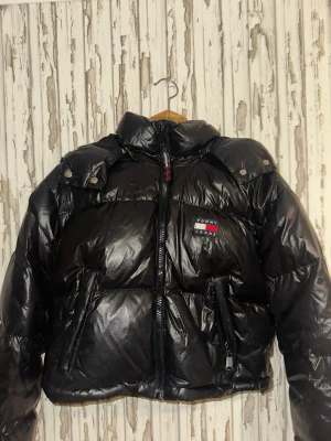 Svart pufferjacka Tommy Jeans S - Snygg svart pufferjacka från Tommy Jeans, modell The Alaska Puffer. Jackan har glansig yta, huva, dragkedja framtill och två fickor med dragkedja. Ikonisk Tommy Jeans-logga på bröstet och ryggen. Perfekt för kalla dagar. Man får även med 2 till jackor, rosa är ifrån SHEIN och den beige är från H&M divided.