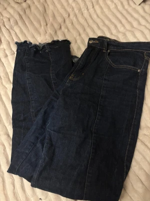 Mörkblå jeans med rå kant från Jack & Jones - Snygga mörkblå jeans från Gina Tricot med klassisk femficksdesign och kontrastsömmar. Jeansen har rak passform och en rå, fransig kant nedtill som ger en cool edge. Perfekta för dig som gillar en enkel men trendig look. Byxorna har en söm längs med benet. Kommer ej till användning 