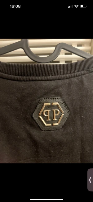 Svart långärmad Philipp Plein tröja XL - Cool svart långärmad tröja från Philipp Plein i bomull, med stor döskalleprint och röd text framtill. Snygga ribbade muddar och PP-logga i nacken. Perfekt för dig som gillar edgy streetwear och vill sticka ut.