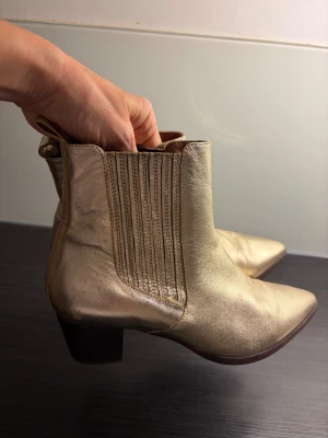 Supercoola skinnboots i guld - Snygga guldiga boots med spetsig tå och låg klack. Bekväma och snygga - perfekt till festklädseln! Små färgskav på insidan, se bild. Inget som syns när man har dem på.