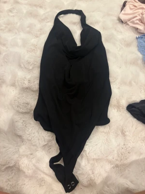 Svart halterneck body från Stradivarius - Snygg svart body från Stradivarius i halterneck-modell med knyt i nacken. Stilren och enkel design. Materialet är mjukt och stretchigt syntet för skön passform.