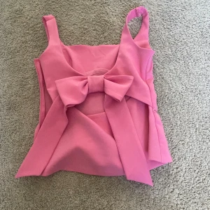 Rosa linnetopp med stor rosett Zara - Supersöt rosa linnetopp från Zara med breda axelband, fyrkantig urringning och en stor rosett i ryggen. Toppen har figurnära passform och är tillverkad i ett slätt, något stretchigt material. Tyvärr för liten för mig. Den har dock en liten fläck som jag tror inte går bort 