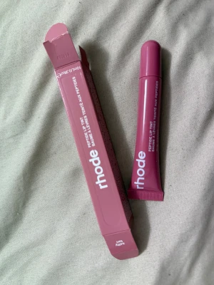 Rhode Peptide Lip Tint i färgen 'Salty' - Säljer en Rhode Peptide Lip Tint i färgen 'Salty', en snygg mörkrosa nyans. Kommer i en praktisk tub med matchande förpackning, perfekt för att ge läpparna både färg och fukt. Formulan innehåller peptider för extra vård och glans.