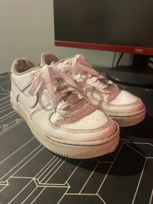 Nike Air Force 1 vita sneakers - Klassiska Nike Air Force 1 sneakers i helvitt skinn med rund tå och platt sula. Skorna har perforerade detaljer på tån, tydliga sömmar och breda vita skosnören. Swoosh-loggan syns på sidorna och AIR-tryck på hälen. Perfekt för dig som gillar streetstyle. Endast några hål som lätt går att fixa så att jag tänker ett pris på 150 kr så får vi se vad ni vill ge. Ge gärna pris förslag 