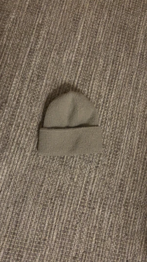 Beige stickad mössa  - En enkel och stilren beige stickad mössa med uppvikt kant. Perfekt för att hålla värmen under kyliga dagar och passar till de flesta outfits. Mjuk och skön känsla tack vare det stickade materialet.