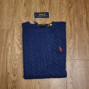 Marinblå kabelstickad tröja Polo Ralph Lauren (i både M och L) - Kabelstickad marinblå tröja från Polo Ralph Lauren med rund halsringning och klassisk röd broderad logga på bröstet. Tröjan har lång ärm och ribbade muddar, perfekt för en stilren och tidlös look. Pris kan diskuteras!!!