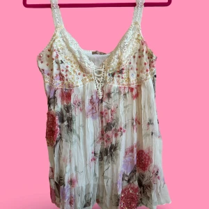 Blommig linnetopp med paljetter och spets - Superfin linnetopp med blommigt mönster i rosa, lila och beige toner. Toppen har spetsdetaljer på axelbanden och upptill, samt glittrande paljetter och snörning vid bysten. 