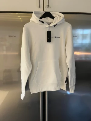Vit hoodie från Sail Racing - Vit hoodie från Sail Racing med logga på bröstet. Tröjan har en stor magficka, samt en liten logga på huvan baktill. Mjuk bomullskänsla och klassisk passform, perfekt för chill dagar. Aldrig använd. Nypris 1299kr 