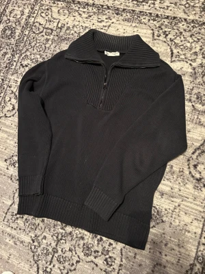 Svart stickad half zip tröja från Zara - Svart stickad tröja från Zara med ribbad krage och half zip-dragkedja framtill. Tröjan har långärmad passform och breda muddar vid ärmslut och nederkant. Perfekt för dig som gillar en clean och chill stil.
