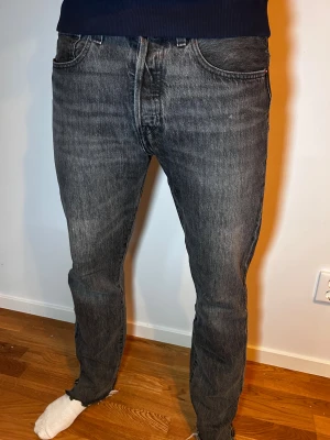 Levi's 501 grå jeans W32 L34 - Säljer ett par Levi's 501 jeans i snygg grå tvätt med klassisk rak passform. Jeansen har fem fickor, knappgylf och slitna benslut för en cool vibe. Perfekt för dig som gillar tidlös stil med en modern touch.