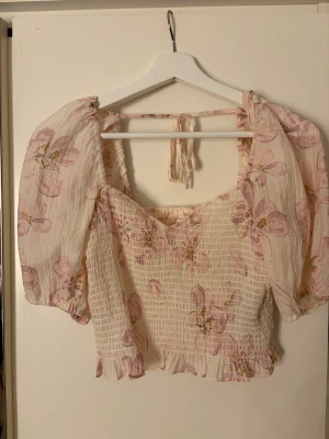 Blommig blus med puffärmar och knyt - Supersöt blommig blus i ljusbeige med rosa och gula blommor. I storlek xs men passar mig som har s superbra också! Använd väldigt sparsamt