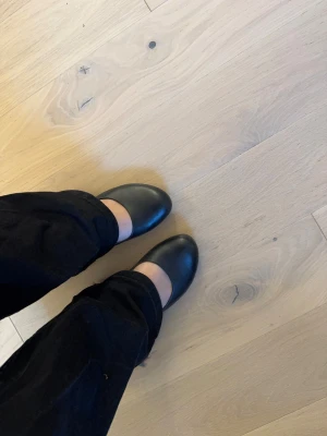 Svarta Vagabond pumps med kilklack - Snygga svarta pumps från Vagabond i storlek 37. Skorna har rund tå, kilklack i trälook och är tillverkade i skinn. Insidan har ett blommigt mönster som ger extra stilpoäng. Perfekta för dig som gillar klassisk och clean design.