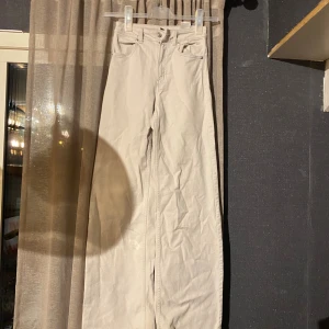 Beiga wide jeans från H&M Divided - Snygga beiga jeans från H&M Divided i storlek 32. Modellen har breda ben och klassisk femficksdesign. Byxorna är tillverkade i bomull och har en ljus beige ton som passar till det mesta. Perfekta för dig som gillar en avslappnad och trendig look. Har en vit fläck nere vid byx benet.