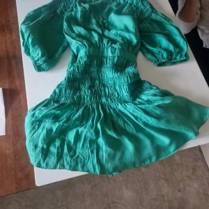 Turkos kortklänning från Ted Baker - Supersöt turkos kortklänning från Ted Baker med puffiga korta ärmar och smockad midja. Klänningen har en flowy kjol och är tillverkad i ett lätt, svalt material som känns lyxigt mot huden. Perfekt för dig som vill sticka ut med färg och stil. Exklusive Ted Baker klänning!