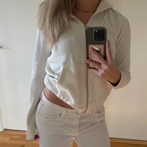 Vit hoodie med dragkedja och huva - Säljer en stilren vit hoodie med dragkedja och huva. Tröjan har långa ärmar, ribbade muddar och två fickor framtill. Perfekt för en chill och avslappnad look. Gjord i mjuk bomull för extra komfort.