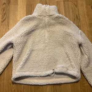 Beige fleece-tröja från Bik Bok - Mjuk och fluffig beige fleece-tröja från Bik Bok med hög krage och half zip. Tröjan har lång ärm och dragsko nertill för en snygg passform. Perfekt för kyliga dagar när du vill vara både varm och stylish.