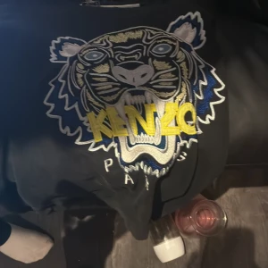 Svart Kenzo sweatshirt med tiger - Cool svart sweatshirt från Kenzo med stort broderat tigerhuvud i blått, vitt, gult och beige på bröstet. Kenzo-loggan i gult broderi. Perfekt statement-plagg för dig som vill sticka ut.