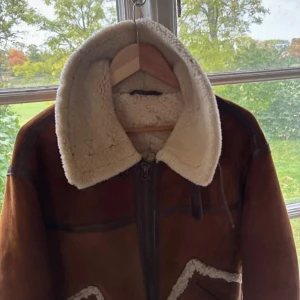 Brun pälsjacka från Chevignon - Säljer en brun pälsjacka från Chevignon med krämvit teddyfoder och stora fickor med pälsdetaljer. Jackan har dragkedja framtill, bred krage och muddar i samma mjuka material. Perfekt för kalla dagar och riktigt snygg vintage vibe.