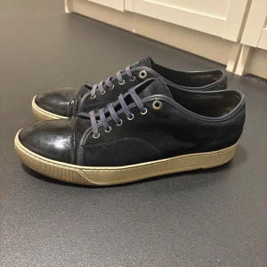 Mörkblå sneakers från Lanvin med lackad tå - Snygga mörkblå sneakers från Lanvin med klassisk och snygg look. Skorna har en lackad tå, ovandel i mocka, samt vita gummisulor. Mörkblå snörning och diskreta metalldetaljer vid snörhålen ger en stilren look. Dem är lite slitna under och några små repor på lacken men annars väldigt fina, också röd färg finns på vänstra skons snörning (bild 5) storlek 44 (UK) 10 funkar både 44 och 45. Priset kan gå ner vid snabb affär. (DUSTBAG INGÅR!!!!!)