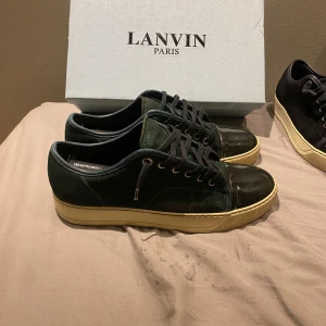 Lanvin gröna sneakers mocka och lack - Snygga sneakers från Lanvin i mörkgrönt mocka med lackad tå och svarta snören. Skorna har en beige platt sula och metallfärgade öljetter. Perfekta för dig som gillar exklusiva och stilrena detaljer. Storlek uk 6 vilket motsvarar 41/42