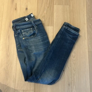 Blå Replay jeans Anbass - Snygga blå jeans från Replay med slim passform och klassiska fem fickor. Jeansen har slitningar och ljusare partier för en cool, använd look. De är tillverkade i stretchigt denim och har detaljerade bakfickor med Replay-logga. Strl: W30 L32. Tveka inte på att hör av er vid fler bilder!