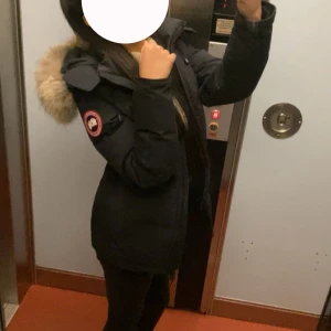 Svart dunjacka Canada Goose med pälskrage - Säljer!!!Säljer en svart dunjacka från Canada Goose med ikonisk patch på ärmen och fluffig pälskant på huvan. Jackan har dragkedja framtill, långa ärmar och en figurnära passform. INTRESSEKOLL! Köp inte! 