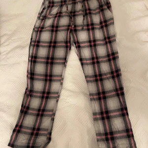 Rutiga pyjamasbyxor  - Säljer ett par rutiga pyjamasbyxor med svart, grått och rosa mönster. Byxorna har resår och snörning i midjan. Perfekt mjukisplagg