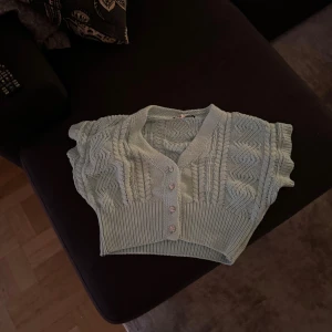 Ljusblå stickad bolerotopp från Zara - Supersöt ljusblå stickad bolerotopp från Zara med korta ärmar och v-ringning. Toppen har ett snyggt stickat mönster, ribbad nederkant och fyra glittriga knappar framtill. Perfekt att slänga över en t-shirt eller klänning för en extra touch.