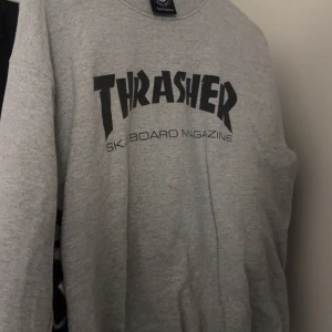 Grå Thrasher sweatshirt - Säljer en grå sweatshirt från Thrasher med klassisk svart logga på bröstet. Tröjan har rund halsringning och långa ärmar, perfekt för en avslappnad streetwear-look.