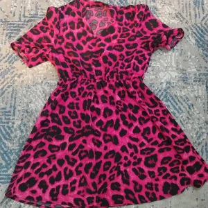 Rosa leopardmönstrad kortklänning - Säljer en riktigt cool kortklänning med leopardmönster i rosa och svart. Klänningen har v-ringning och korta ärmar, samt en markerad midja som ger en snygg siluett. Perfekt för dig som vill sticka ut och älskar djurmönster!